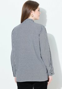 Schwarz-weiß karierte Button-Up-Bluse mit langen Ärmeln, lockerer Passform, Kragen und umgeschlagenen Handgelenken, von hinten auf einem hellen Hintergrund gezeigt.