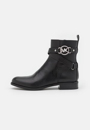 Botte d'ankle noire en cuir avec un talon bas, sangle autour de la tige dotée d'une boucle circulaire argentée portant le logo "MK" sur le côté extérieur.