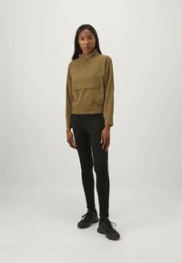 Olivově zelený pulovr s vysokým límcem a polovičním zipem, s přední kapsou. V kombinaci s černými legínami a tmavými teniskami.