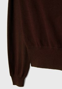 Manche et ourlet de pull tricoté marron foncé avec poignets en côte, présentés sur un fond clair.