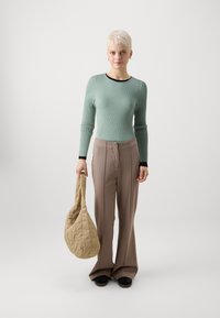 Minttuvihreä ryppyinen pitkähihainen paita mustilla reunuksilla, beige leveälahkeiset housut ja vanutettu beige olkalaukku, yhdistettynä mustiin kenkiin.