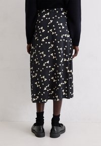 Schwarzer Midirock mit weißen Blumenmustern, plissiertes Design, glatte Textur, kombiniert mit schwarzen Schuhen und gerippten schwarzen Socken.