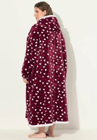 Plüsch-Hoodie-Decke in Burgunderrot mit einem Muster aus weißen und hellrosa Herzen; hat eine weiche Textur und einen weißen Saum am Rand.
