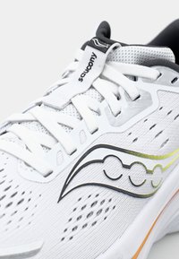 Weiße Sportschuhe mit Mesh-Obermaterial, schwarzen und gelben Akzenten, runder Zehenpartie, flachen Schnürsenkeln und auffälligem Markenlogo auf der Zunge.