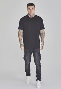 Black cotton t-shirt with short sleeves and a crew neck, paired with dark gray cargo jeans featuring side pockets, worn with white sneakers.