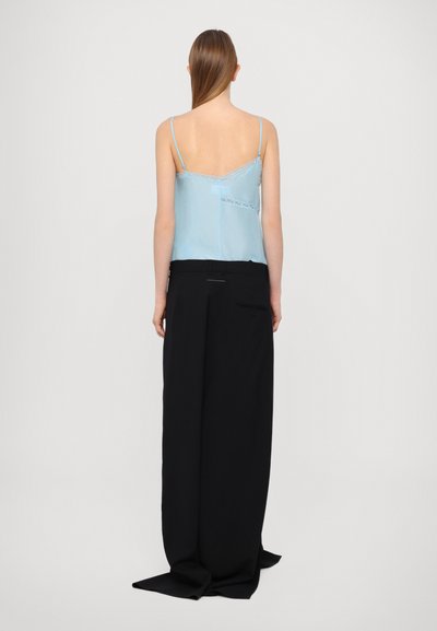 Helleblaue Satin-Camisole mit Spitzendetails, kombiniert mit locker sitzenden, hoch taillierten schwarzen Hosen. Minimalistisches Design mit geraden Linien.
