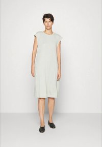 Vestido de algodão cinza claro com mangas em cap sleeve, comprimento até ao joelho, design fluido, com bolsos laterais e decote redondo. Usado com sapatos planos pretos.