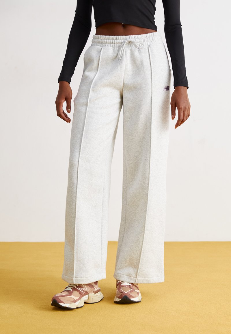 Lichtgrijze, wijde sweatpants met een trekkoord in de taille en voornaad. Gecombineerd met gemusterde lichtroze en crème sport schoenen.