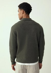 Ciemnozielony prążkowany sweter z dzianiny z kołnierzem, o teksturowanym wykończeniu i luźnym kroju. Długie rękawy z mankietami oraz dłuższy tył.