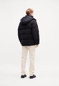 Black puffer jacket with a hood, featuring a quilted design and a loose fit. Worn over light beige pants and black shoes, showing a casual look.