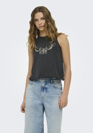 Joven mujer con cabello ondulado que lleva una camiseta sin mangas negra con diseño de "Rock Roll" y alas, combinada con vaqueros de cintura alta de color azul claro.