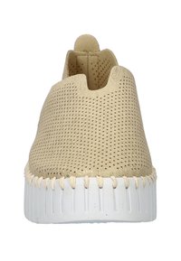 Zapatilla color beige tipo slip-on con parte superior de malla transpirable, puntera redondeada y suela de goma blanca que presenta una costura texturizada en zigzag alrededor del borde.
