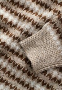 Strickpullover aus weicher, beiger Wolle mit einem Hahnentritt-Muster in Braun. Gerippte Ärmelabschlüsse mit einer strukturierten Oberfläche.