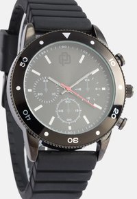 Melns analogais pulkstenis ar gumijas siksniņu. Tam ir tumša sejas daļa ar baltām un sarkanām akcentiem, trīs apakšdialiem un grozāmu rāmīti.