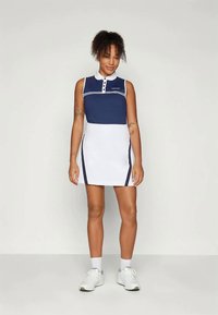 Námořnicko-modrá a bílá polo šaty s límcem, třemi knoflíky a bočními pruhy. Materiál se zdá být hladký s přiléhavým designem.