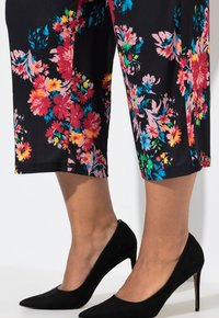 Bloemige cropped broeken met een zwarte achtergrond, versierd met levendige roze, gele en blauwe bloemen. Gecombineerd met zwarte suède hoge hakken.