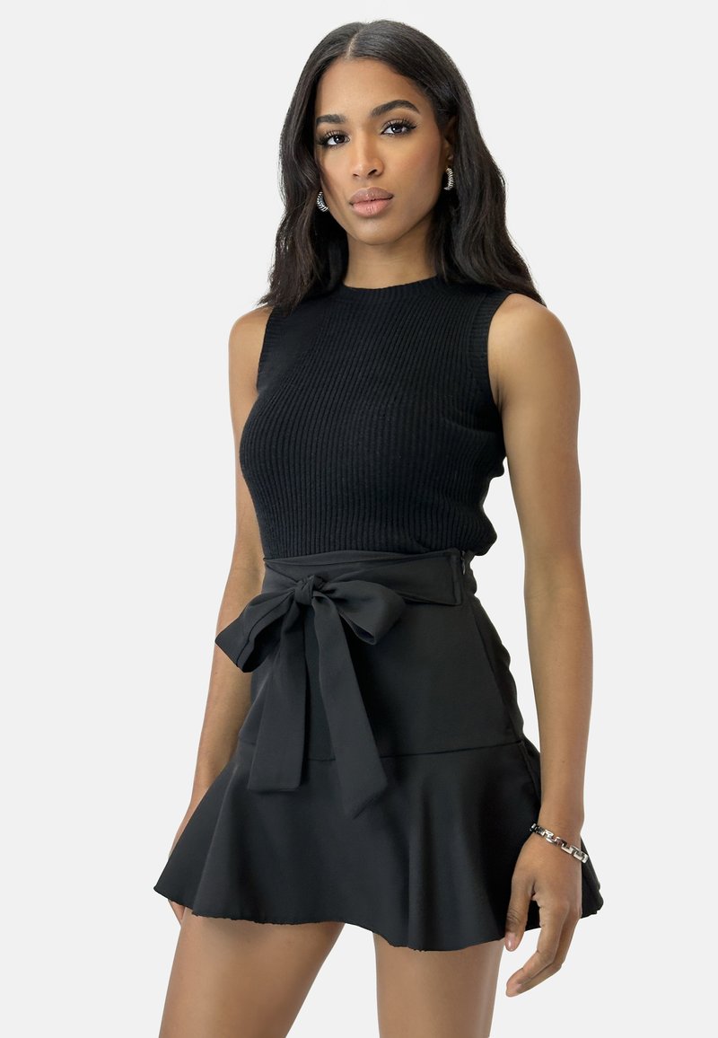 Top sin mangas de canalé negro combinado con una falda negra acampanada que presenta un lazo en la parte delantera. Textura suave con una línea de cintura ajustada.