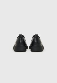 Une paire de chaussures à plateforme noires en cuir montrées de dos, avec des semelles épaisses et des détails de couture sur un fond blanc uni.
