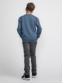 Sudadera de manga larga azul claro con cuello redondo, combinada con jeans gris oscuro. Zapatillas negras y blancas completan el atuendo.
