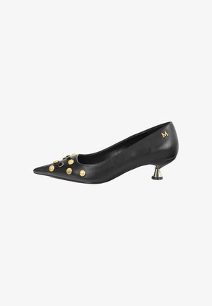 Zapato negro de tacón bajo y punta puntiaguda con tachuelas doradas en la parte delantera y una pequeña letra M dorada cerca del tacón sobre un fondo blanco.
