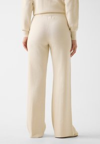Cream-colored, wide-leg pants made of soft fabric. Features a high waist and minimal seams for a smooth silhouette.