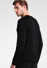 Sort langærmet t-shirt, rund halsudskæring, blødt stof, tætsiddende silhuet, minimalistisk design, ingen synlige mønstre eller detaljer.