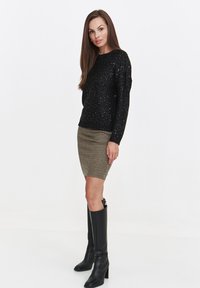 Black sequined sweater with long sleeves paired with a fitted houndstooth skirt. Model wears knee-high black leather boots.