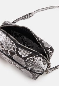 Malá kabelka se vzorem hadí kůže v černobílé barvě, se stříbrným zipem, vnější klopou a nastavitelným popruhem. Disponuje texturovaným povrchem a prostorným interiérem.