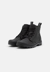 Botas de tobillo negras hechas de cuero texturizado con una suela de goma resistente. Presentan un cierre de cordones en la parte delantera y bucles para facilitar el uso.