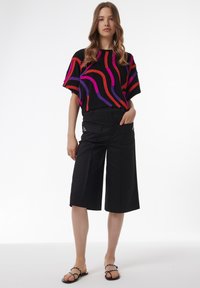 Top corto negro con rayas onduladas moradas y rojas, combinado con shorts negros hasta la rodilla que presentan bolsillos laterales y un hardware detallado.