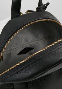 Schwarzer Leder-Rucksack mit Innenraum, der ein Reißverschlussfach, eine strukturierte Innenauskleidung und goldene Reißverschlussakzente aufweist. Glatte Außenseite mit strukturierter Form.