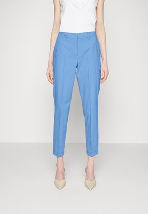 Mujer vistiendo pantalones de sastre azules claros recortados con puños, combinados con tacones beige de punta fina y una blusa sin mangas blanca.