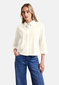 Vit, knappad skjorta med krage och trekvartslånga ärmar; gjord av lätt tyg; kombinerad med blå, vida denimjeans.