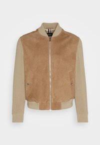 Veste bomber beige avec devant en daim et manches tricotées, col, poignets et bas côtelés, fermeture éclair et poches avant à boutons.