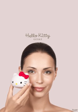 Kvinde med mørkt hår holder hvid Hello Kitty-ansigt med rød sløjfe tæt ved sin kind mod en neutral baggrund.