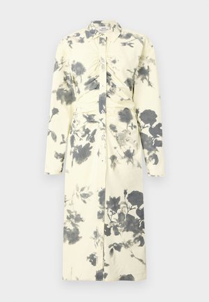 Pitkähihainen, nappi-käytä mekko pehmeässä keltaisessa kankaassa, jossa on musta kukkakuosi ja kerätty yksityiskohta vyötäröllä.