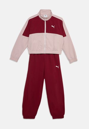 Survêtement Puma bicolore bordeaux et rose clair avec veste zippée et poignets élastiques aux manches et aux pantalons sur fond blanc.