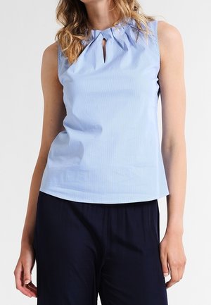 Woman wearing sleeveless light blue pinstriped blouse with gathered neckline and small keyhole, paired with dark navy pants.