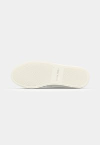Semelle de sneaker blanche avec une surface en caoutchouc texturé, présentant une adhérence à motifs et des détails de marque en relief. Design lisse et plat.