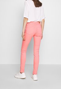 Slim jeans v jasně růžové bavlně, s zadními kapsami, středním pasem a hladkou texturou. Kombinované s bílými teniskami.