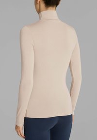 Top a maniche lunghe e collo alto in beige chiaro, realizzato in materiale morbido e elasticizzato. Presenta un design fitted e una texture liscia senza motivi visibili.