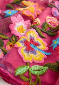 Broderad tyg med rosa bakgrund pryds av livfulla blommönster i olika färger, inklusive blå, gul och gröna blad.