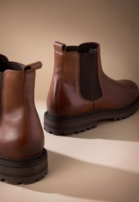 Hnedé kožené Chelsea topánky s robustnou gumovou podrážkou, elastickými bočnými panelmi a pútkami vzadu pre jednoduché obúvanie.