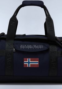 Marinblå duffelväska med förstärkta handtag och en framficka med ett norskt flaggpatch. Materialet har en strukturerad yta; logotypen är präglad.