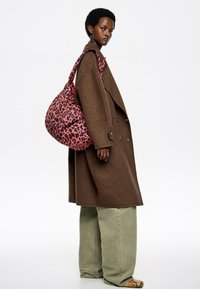 Brązowy, luźny płaszcz, zielone spodnie o szerokich nogawkach oraz różowa torba w panterkę o luźnym kroju i szerokim pasku na ramię.