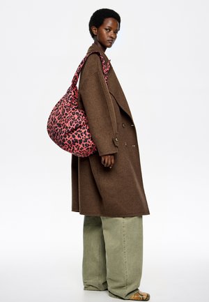 Abrigo marrón oversize, pantalones verdes de pierna ancha y un bolso rosa con estampado de leopardo, de forma blanda y asa ancha para el hombro.