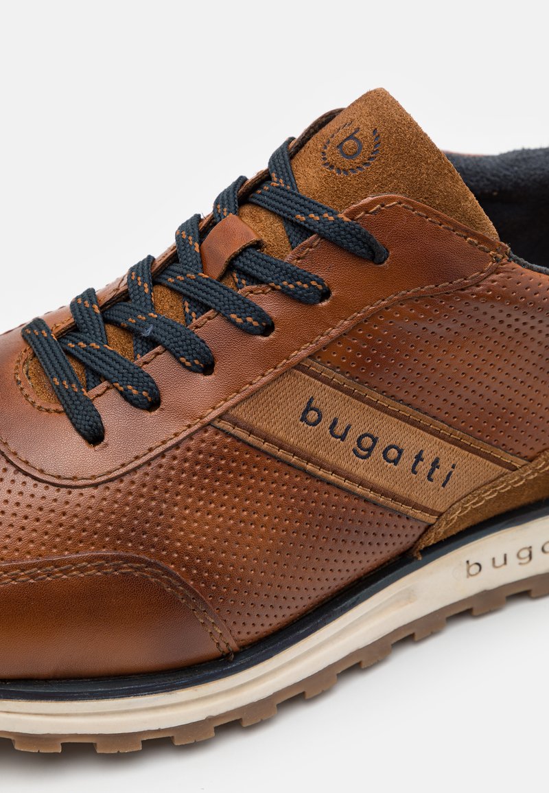 Sneaker en cuir marron avec un design perforé, des accents contrastants en tan, des lacets bleu marine et une semelle en caoutchouc avec la marque "bugatti".