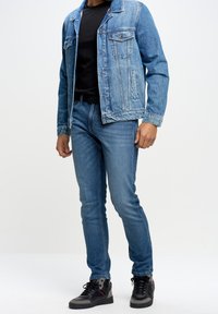 Jeanjacka med ljusblå tvätt, mörk t-shirt, slim-fit blå jeans och svarta sneakers med grå detaljer.