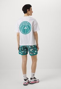 Biała koszulka z grafiką teal okrągłej piłki do koszykówki na plecach. Połączona z tealowymi szortami w kontrastowym wzorze. Czarno-białe sneakersy.