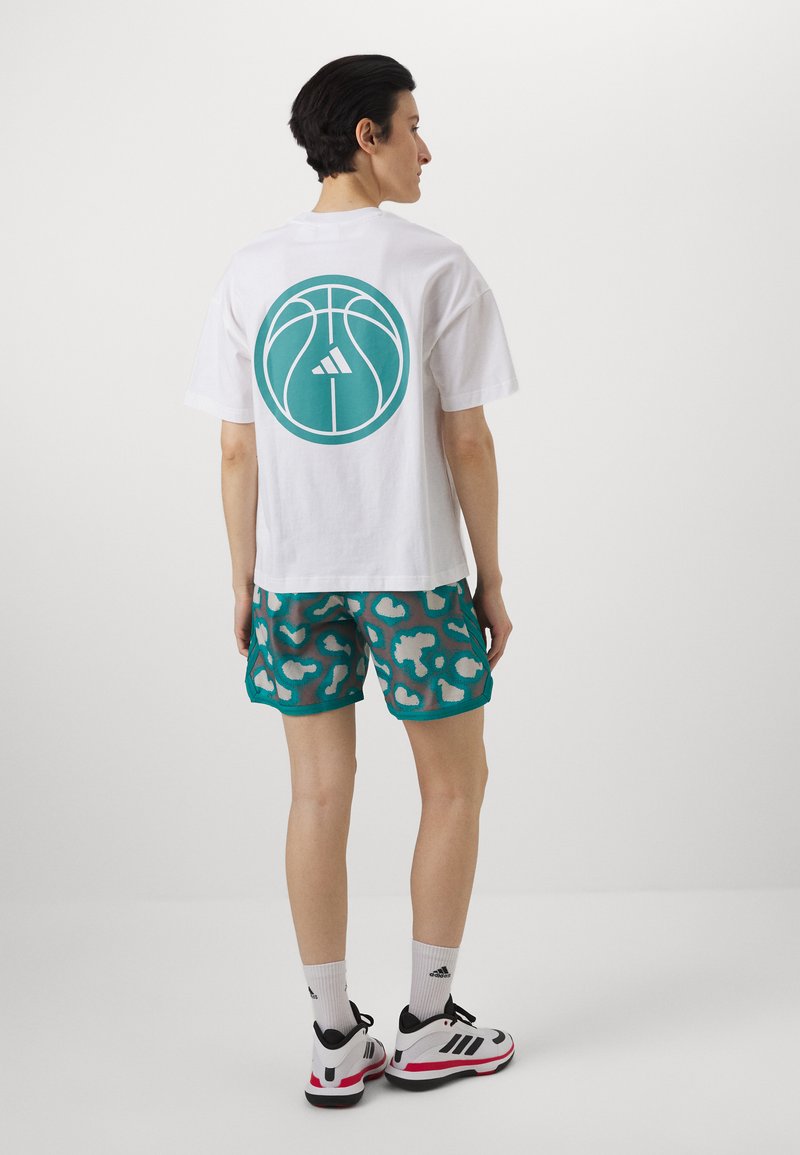 Vit t-shirt med en teal-färgad cirkulär basketgrafik på baksidan. Kombinerad med teal shorts med ett kontrasterande mönster. Svart och vit sneakers.